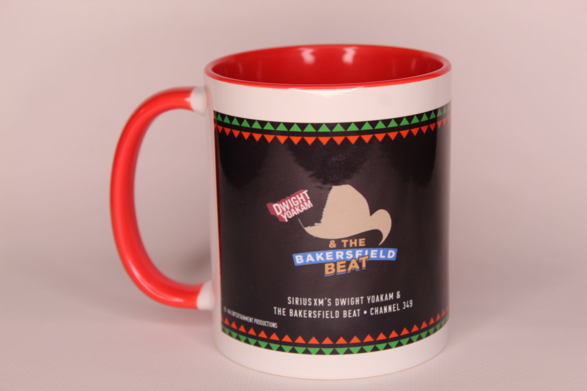 A ceramic mug with a white exterior, red handle and interior, featuring a black wraparound graphic with a cowboy hat silhouette and the text 'Dwight Yoakam & The Bakersfield Beat'.